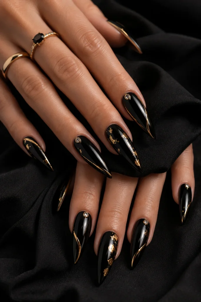 Long black stiletto nails with fine metallic gold accents and foil detail