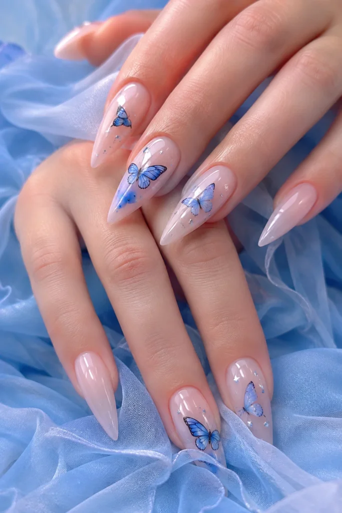 Long stiletto nails with a nude base and delicate hand-painted blue butterflies